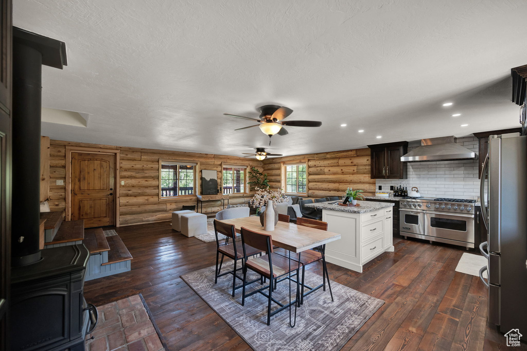 Kitchen with stainless steel appliances, log walls, wall chimney exhaust hood, tasteful backsplash, and ceiling fan