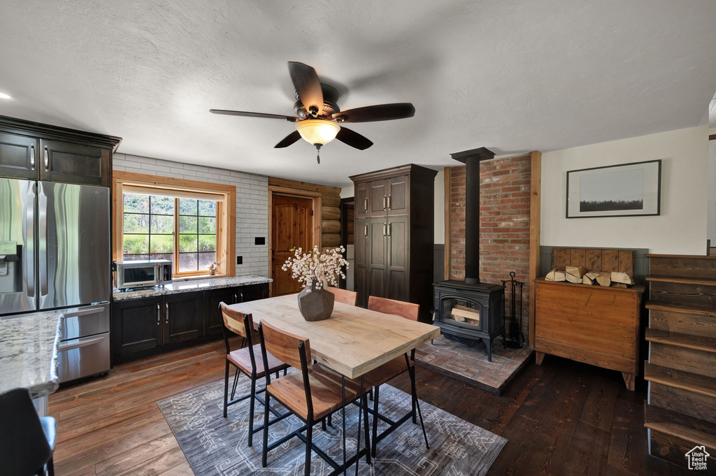 Dining space with brick wall, dark hardwood / wood-style floors, ceiling fan, and a wood stove