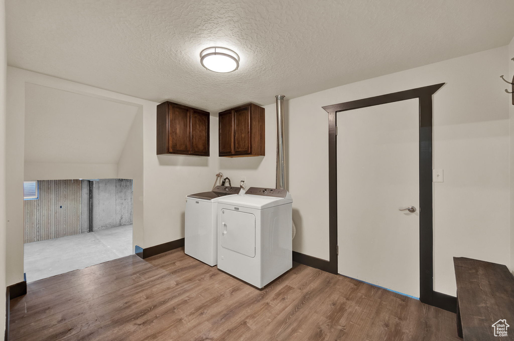 Laundry room with light hardwood / wood-style floors, a textured ceiling, cabinets, and washer and clothes dryer