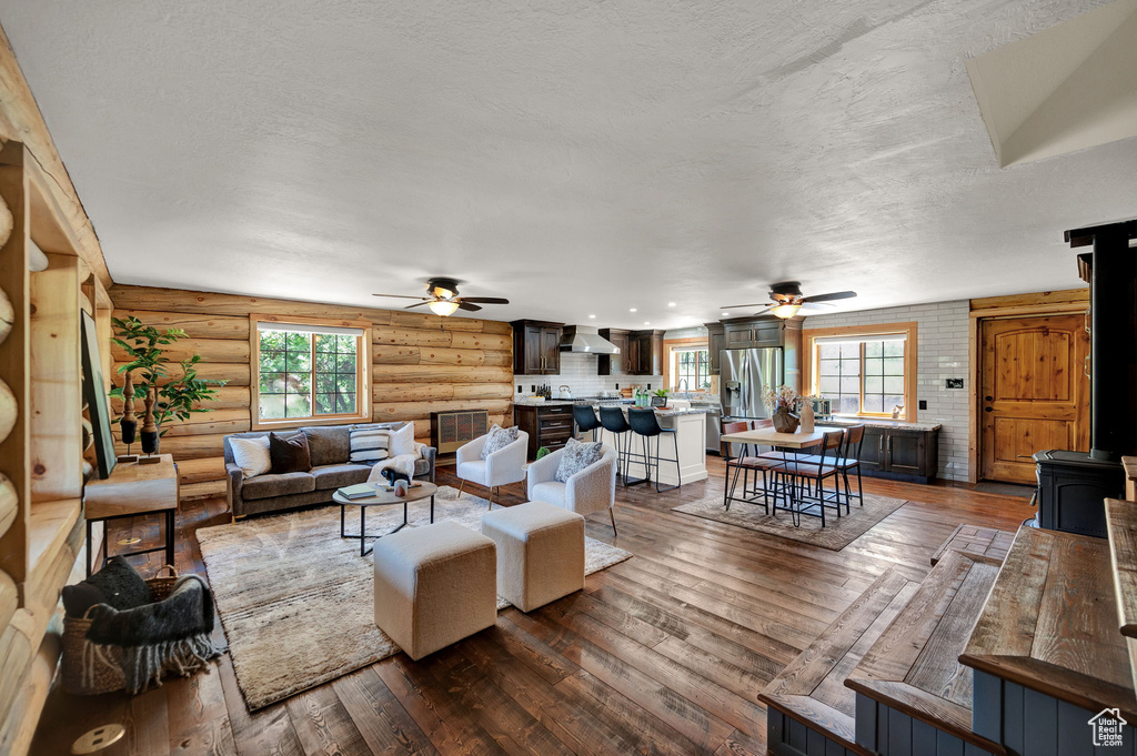 Living room with a textured ceiling, ceiling fan, log walls, and wood-type flooring