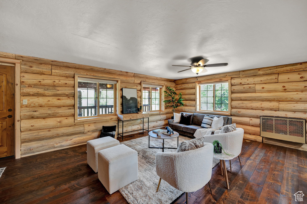 Living room with rustic walls, ceiling fan, and dark hardwood / wood-style floors