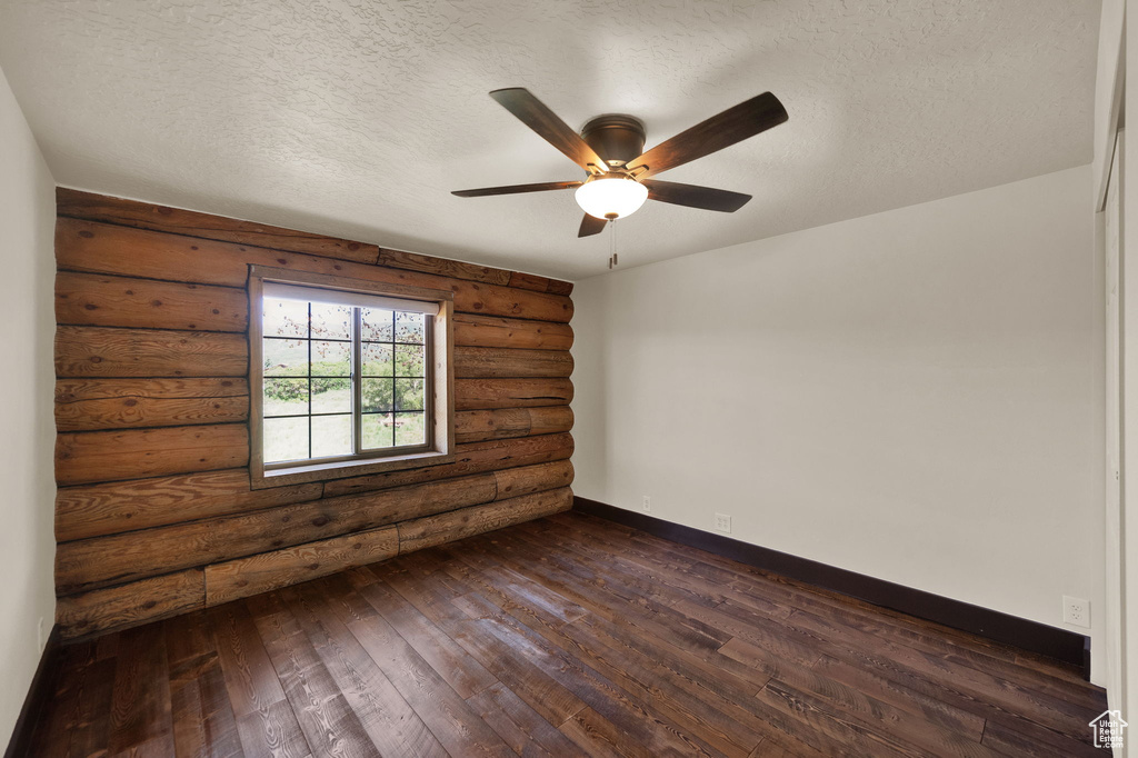 Empty room featuring a textured ceiling, dark wood-type flooring, ceiling fan, and log walls