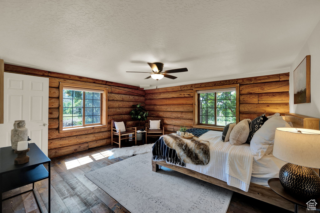 Bedroom with ceiling fan, a textured ceiling, hardwood / wood-style flooring, and rustic walls