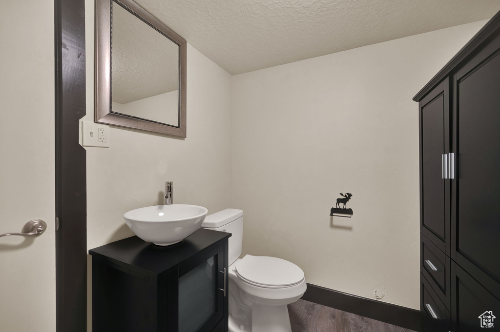 Bathroom with a textured ceiling, toilet, hardwood / wood-style flooring, and vanity