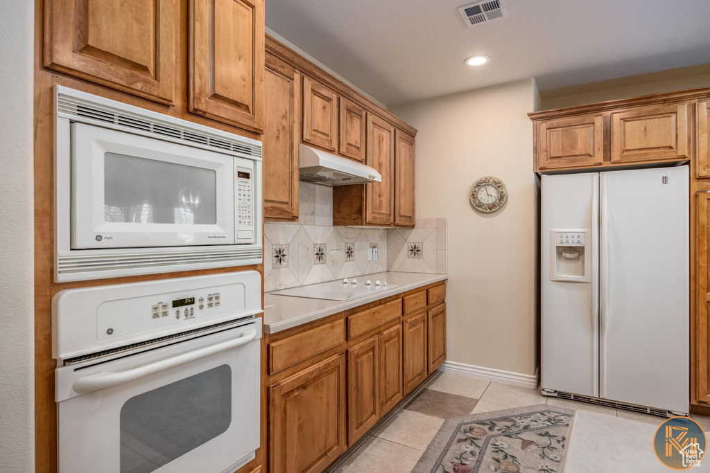 Kitchen with backsplash, white appliances, and light tile floors