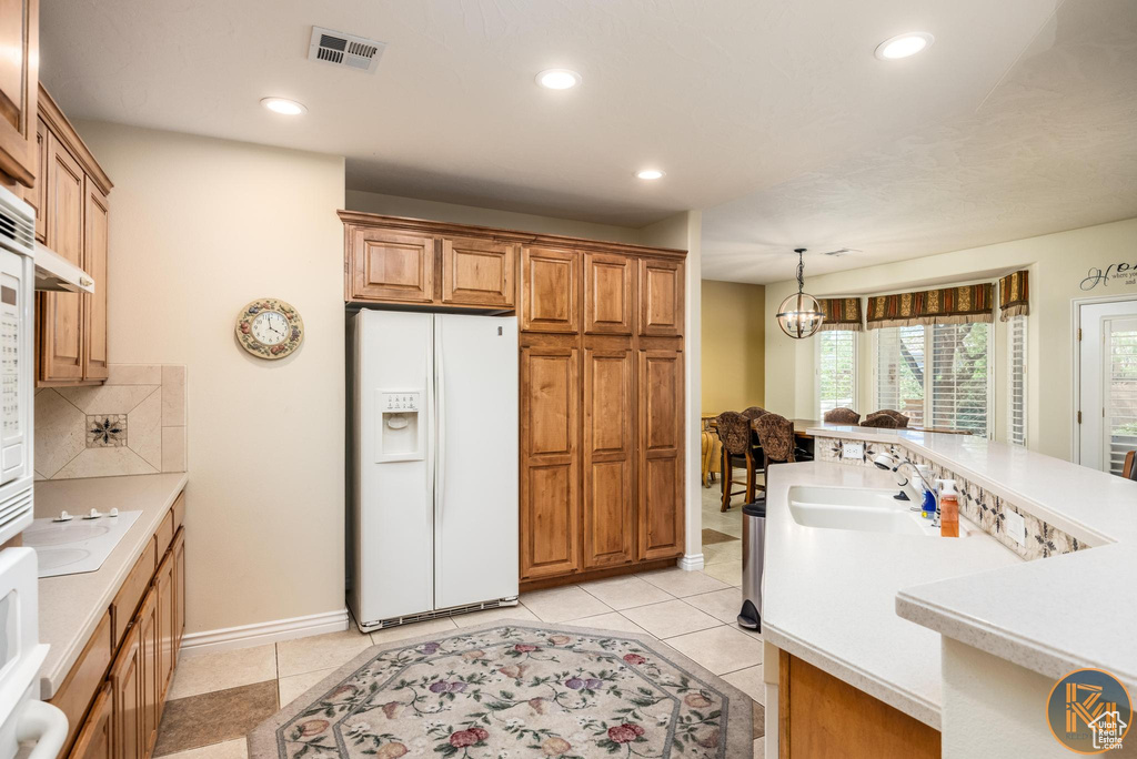 Kitchen with white appliances, light tile flooring, backsplash, hanging light fixtures, and sink