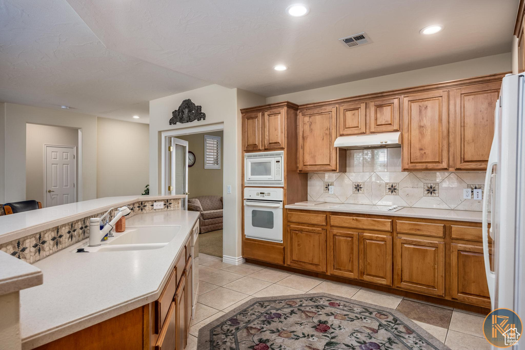 Kitchen with sink, tasteful backsplash, white appliances, and light tile floors