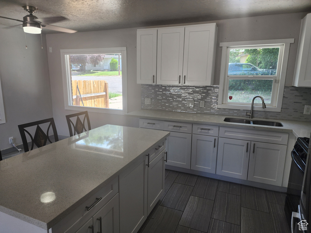 Kitchen with backsplash, ceiling fan, range, a center island, and sink