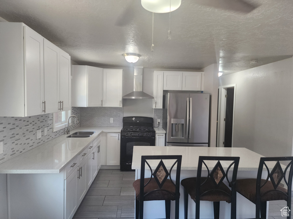 Kitchen featuring wall chimney range hood, tasteful backsplash, white cabinetry, gas stove, and stainless steel fridge