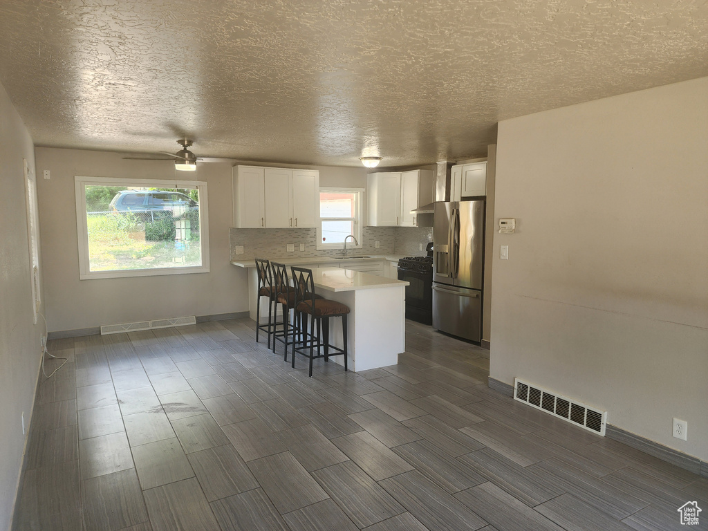 Kitchen with stainless steel fridge, white cabinets, a breakfast bar area, tasteful backsplash, and black range with gas cooktop