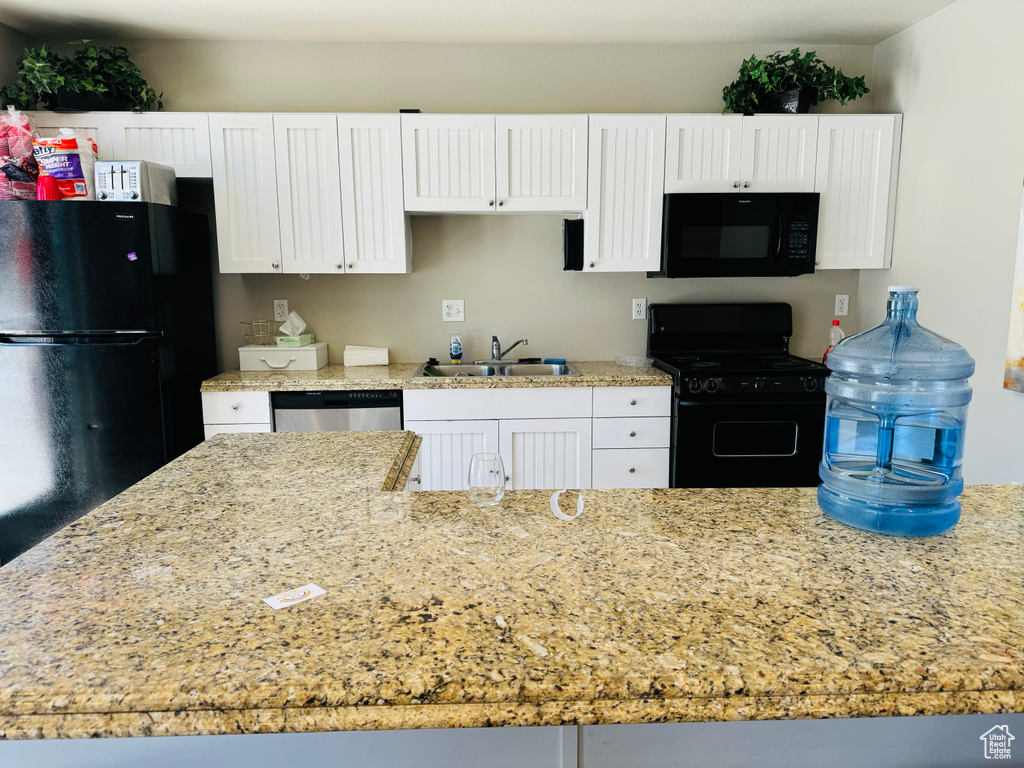 Kitchen featuring black appliances, sink, white cabinetry, and light stone counters