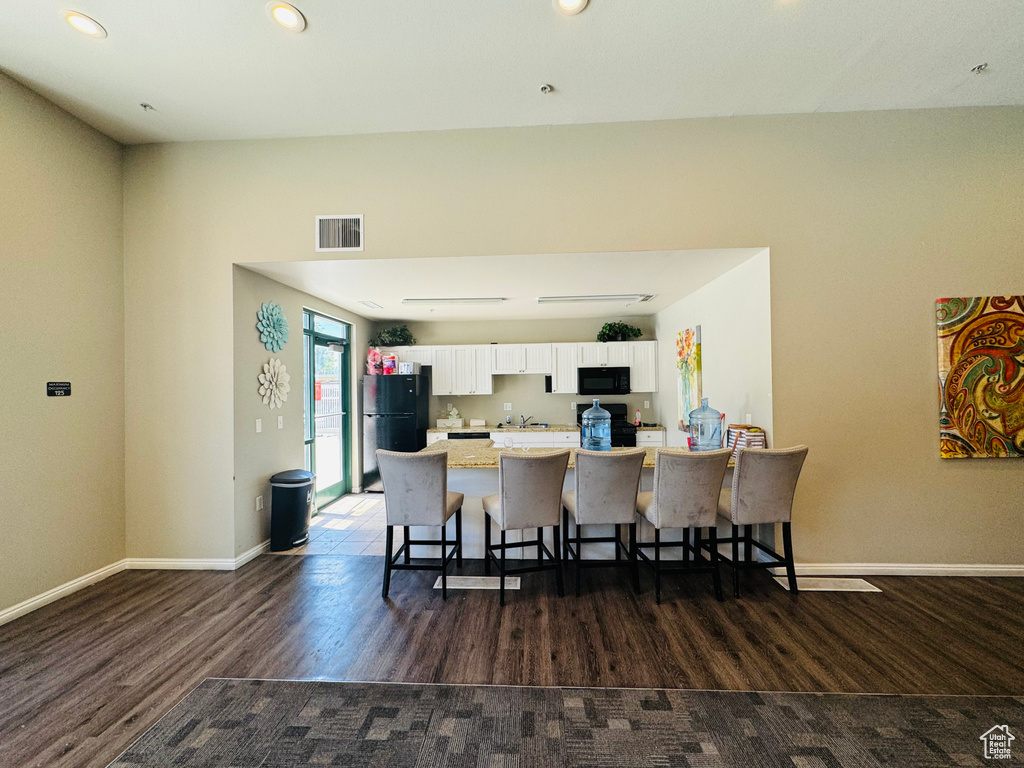 Kitchen featuring a kitchen bar, white cabinetry, hardwood / wood-style flooring, and black appliances