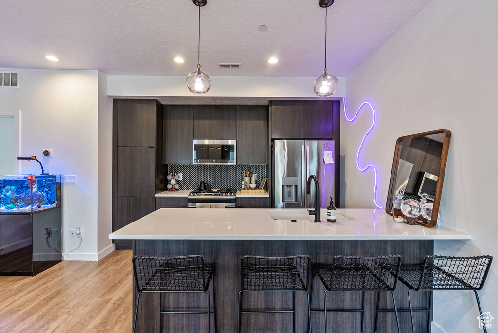 Kitchen featuring light hardwood / wood-style flooring, a kitchen bar, backsplash, and stainless steel appliances