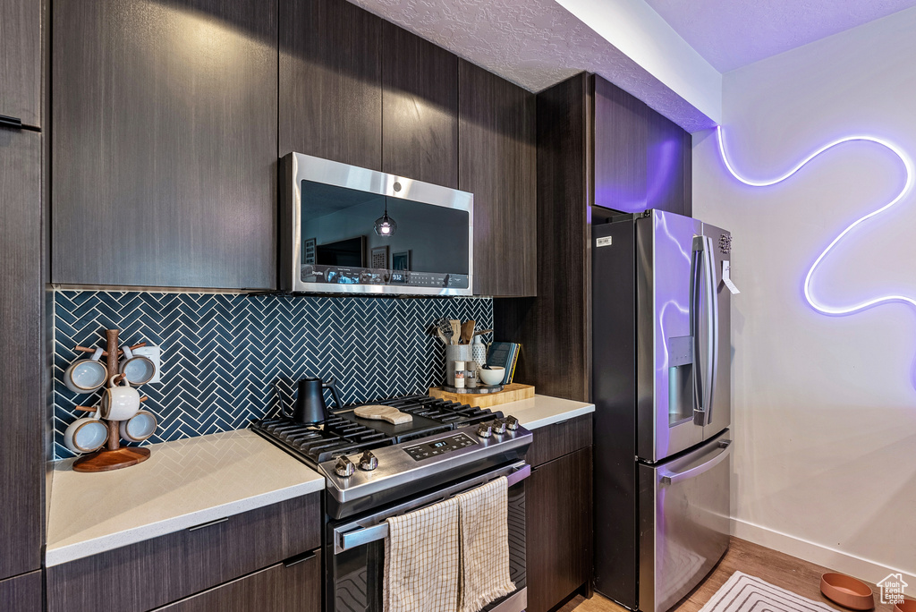 Kitchen with dark brown cabinetry, light hardwood / wood-style flooring, backsplash, and stainless steel appliances