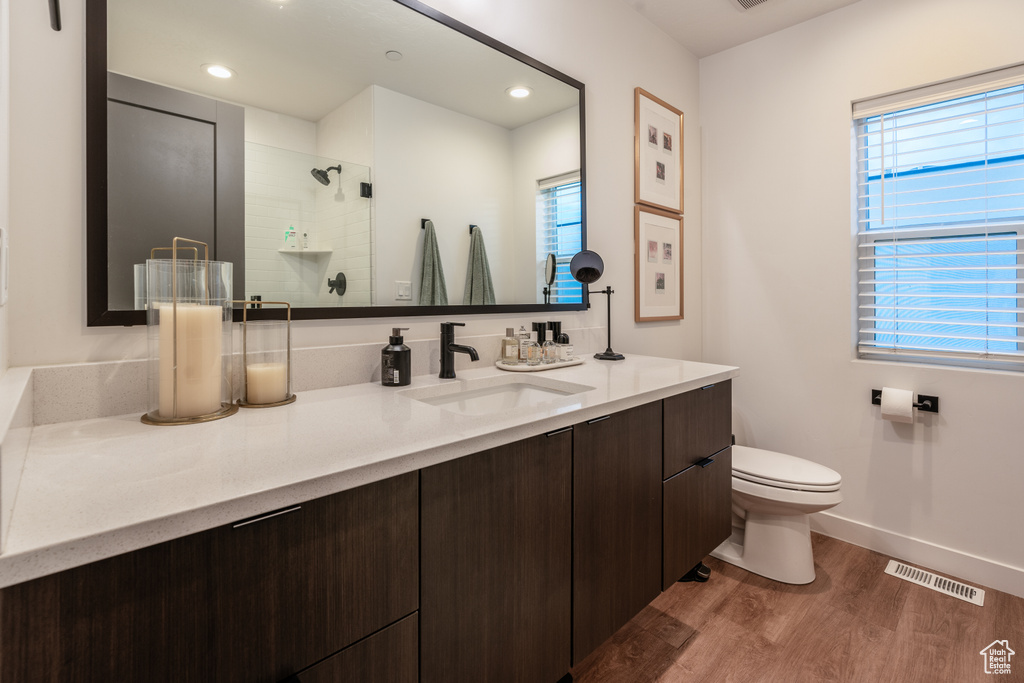 Bathroom with vanity, toilet, wood-type flooring, and a tile shower