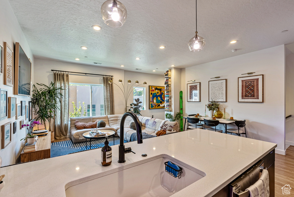 Kitchen featuring sink, hanging light fixtures, stainless steel dishwasher, a textured ceiling, and hardwood / wood-style flooring