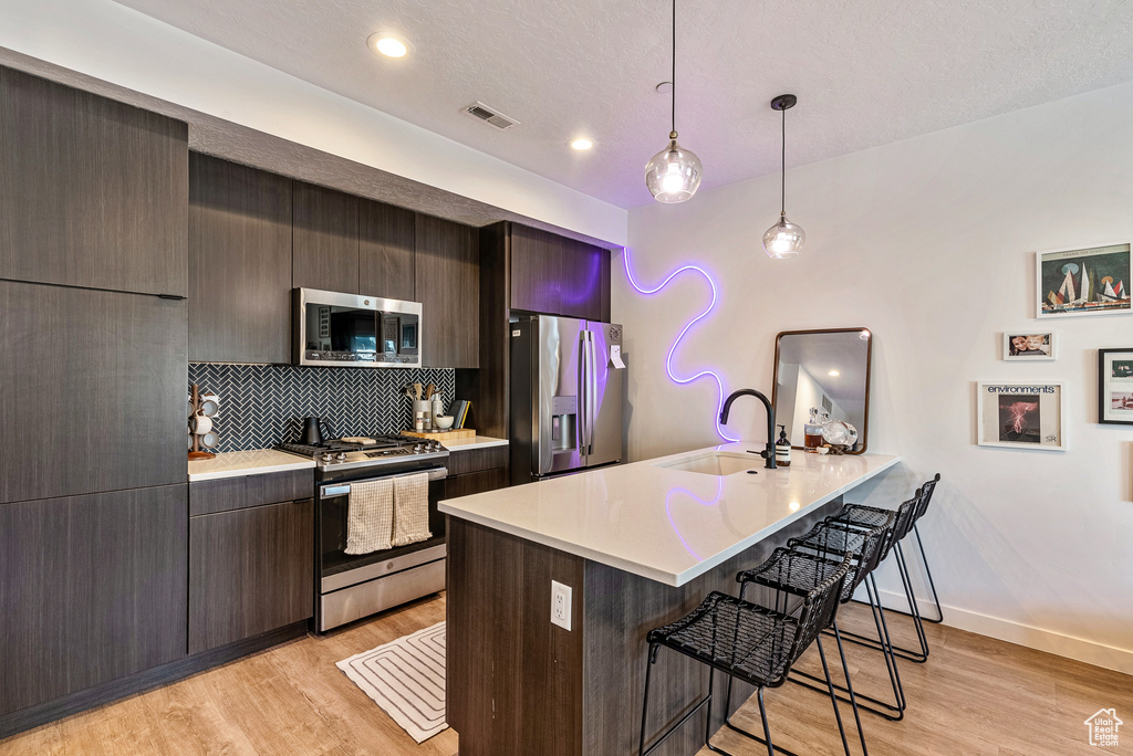 Kitchen featuring light wood-type flooring, backsplash, a kitchen bar, stainless steel appliances, and sink