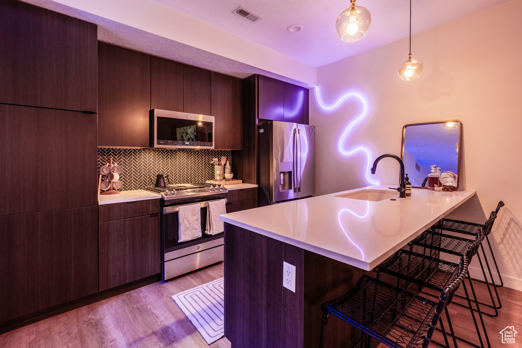 Kitchen featuring a kitchen breakfast bar, light hardwood / wood-style flooring, hanging light fixtures, stainless steel appliances, and sink