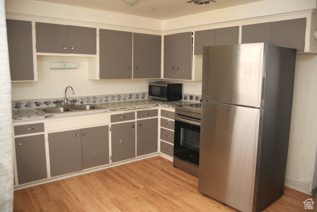 Kitchen featuring stainless steel appliances, gray cabinetry, sink, and light hardwood / wood-style flooring