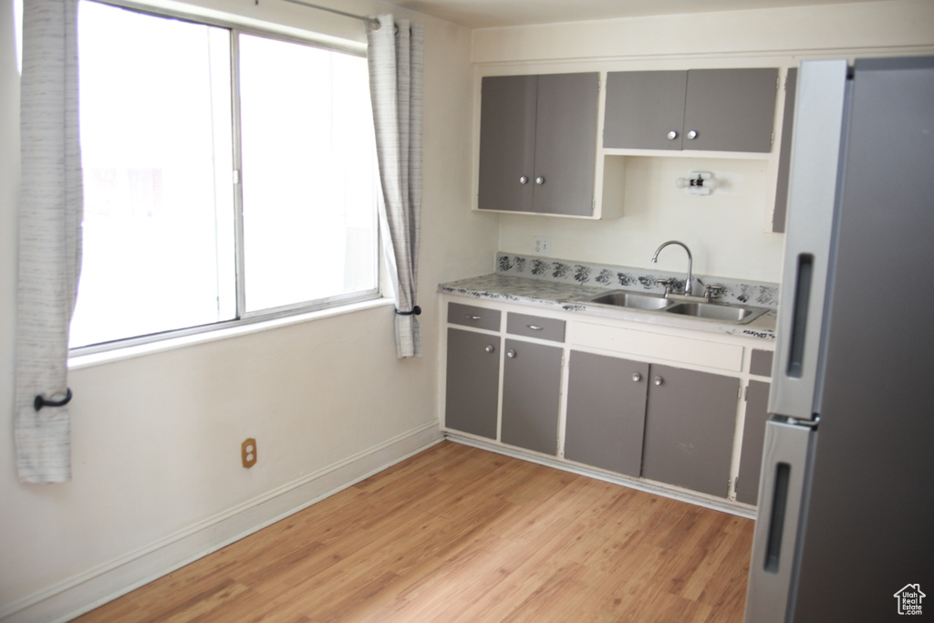 Kitchen with gray cabinetry, sink, white fridge, and light wood-type flooring