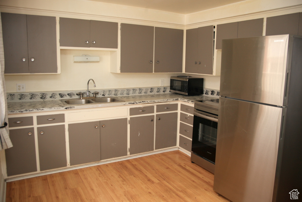 Kitchen with sink, gray cabinets, light wood-type flooring, and appliances with stainless steel finishes