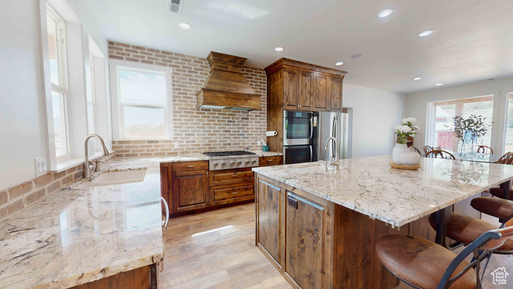 Kitchen with light hardwood / wood-style flooring, custom exhaust hood, a center island, appliances with stainless steel finishes, and a breakfast bar