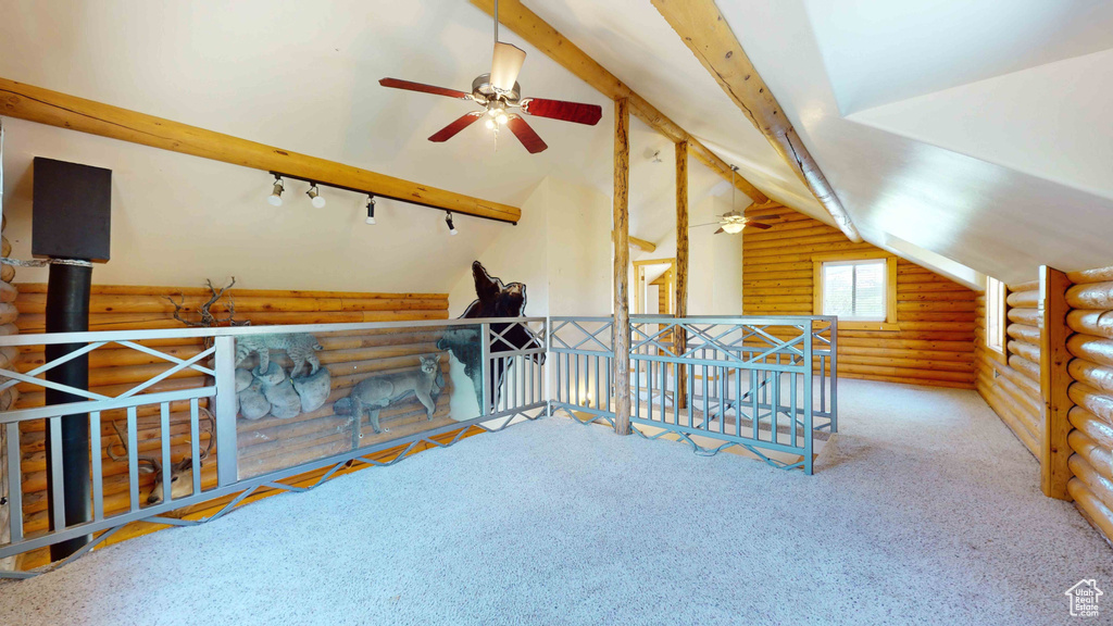Additional living space featuring carpet flooring, rustic walls, lofted ceiling with beams, and ceiling fan