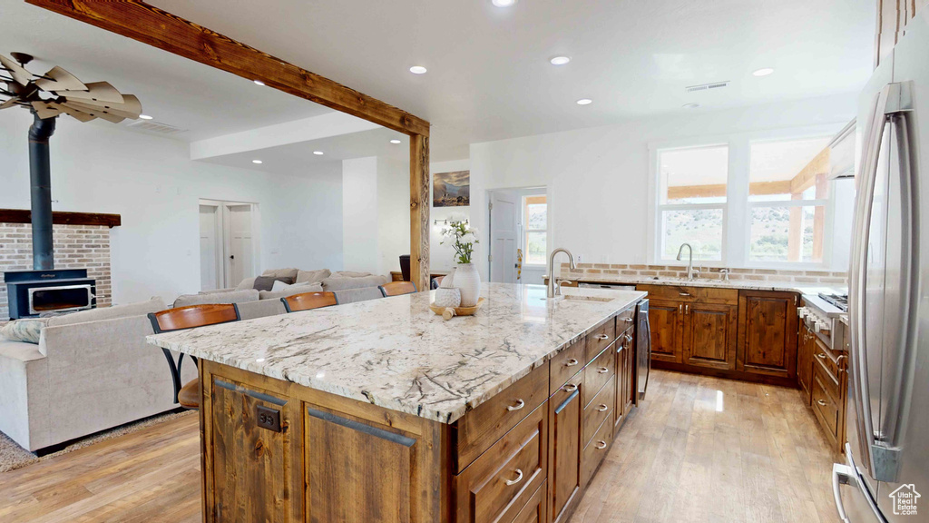 Kitchen featuring ceiling fan, light wood-type flooring, light stone counters, a wood stove, and a kitchen island with sink