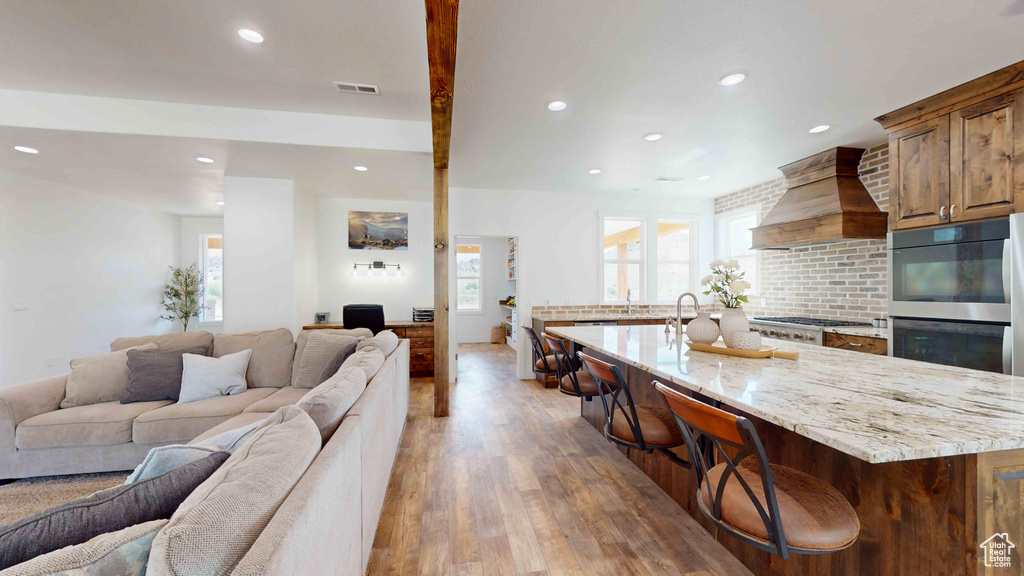 Kitchen with an island with sink, a wealth of natural light, wood-type flooring, and custom range hood