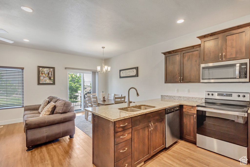 Kitchen with kitchen peninsula, a notable chandelier, light wood-type flooring, appliances with stainless steel finishes, and sink