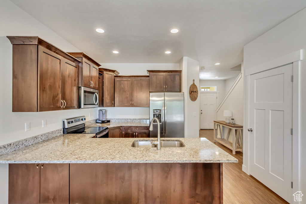 Kitchen with light stone countertops, light wood-type flooring, stainless steel appliances, kitchen peninsula, and sink