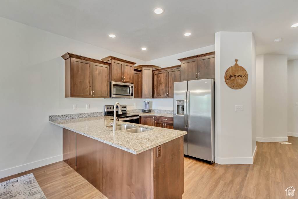 Kitchen featuring light hardwood / wood-style flooring, kitchen peninsula, stainless steel appliances, light stone countertops, and sink