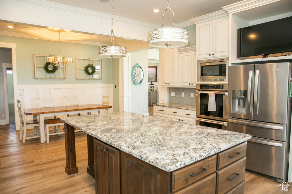 Kitchen featuring tasteful backsplash, light wood-type flooring, ornamental molding, a center island, and appliances with stainless steel finishes