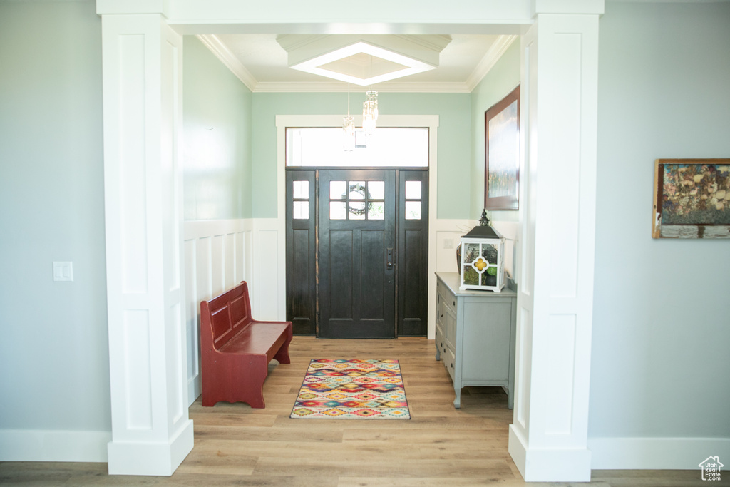 Foyer entrance featuring crown molding, light hardwood / wood-style flooring, and decorative columns