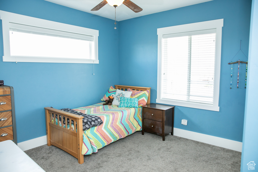 Carpeted bedroom featuring multiple windows and ceiling fan