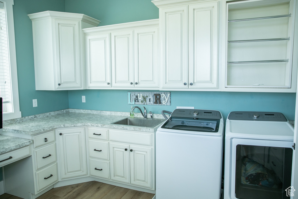 Washroom with cabinets, sink, light hardwood / wood-style flooring, and washing machine and dryer