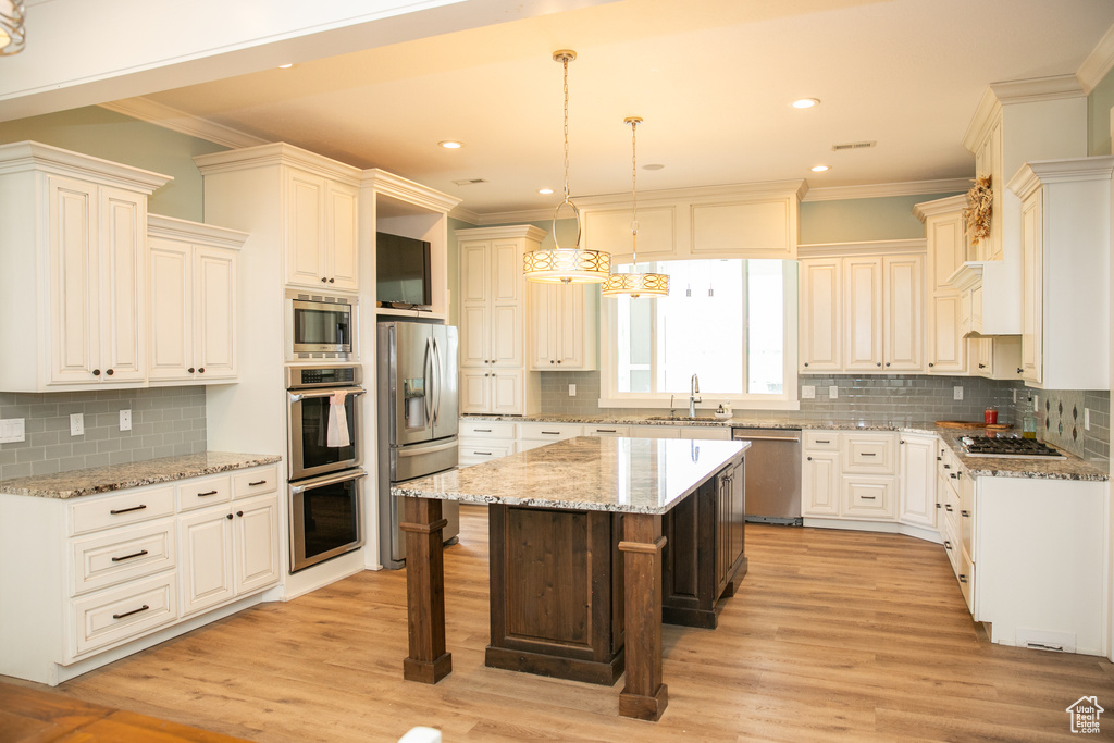 Kitchen featuring appliances with stainless steel finishes, light hardwood / wood-style flooring, hanging light fixtures, backsplash, and a center island