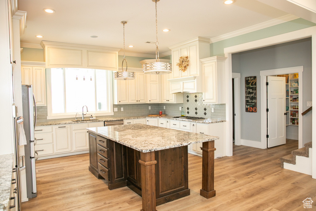 Kitchen featuring decorative light fixtures, light wood-type flooring, sink, a center island, and light stone countertops