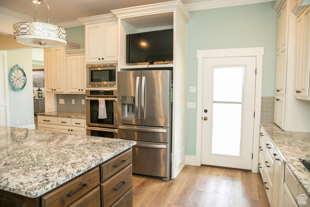 Kitchen with tasteful backsplash, light hardwood / wood-style floors, appliances with stainless steel finishes, and ornamental molding