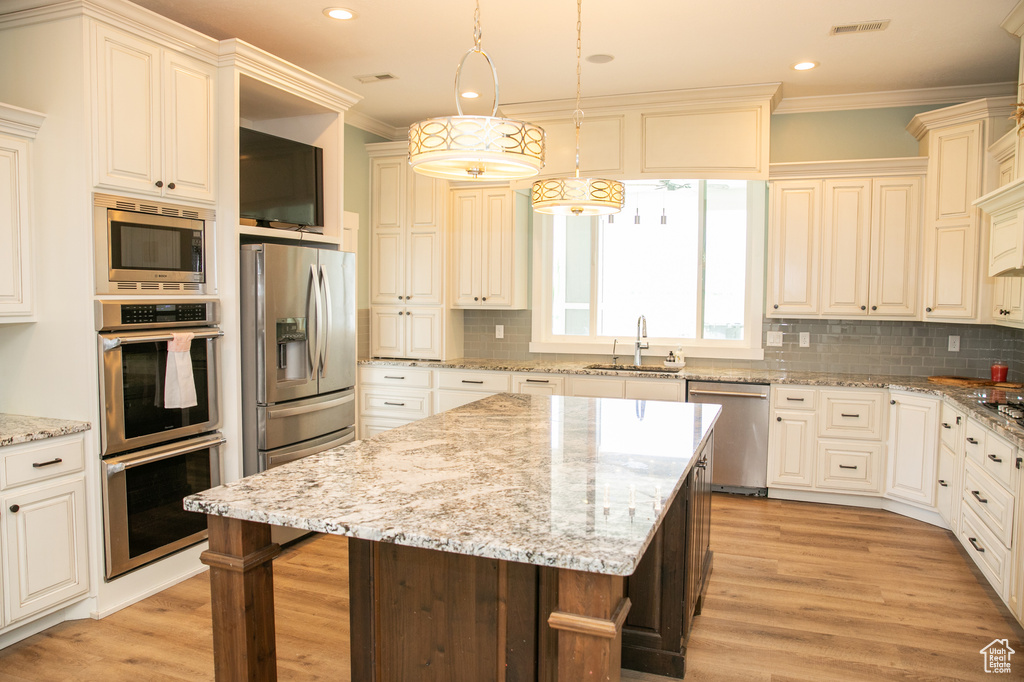 Kitchen with a center island, appliances with stainless steel finishes, decorative backsplash, and decorative light fixtures