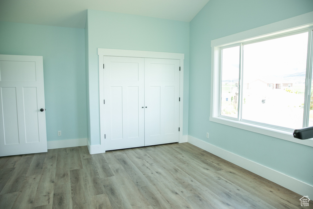 Unfurnished bedroom with hardwood / wood-style flooring, lofted ceiling, and a closet