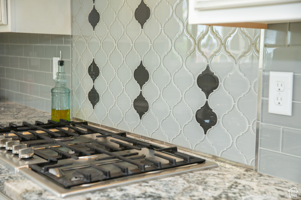 Room details with stainless steel gas cooktop, decorative backsplash, and white cabinetry