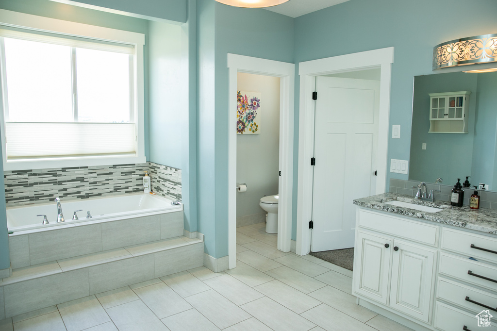 Bathroom featuring vanity, tile patterned floors, tiled bath, and toilet