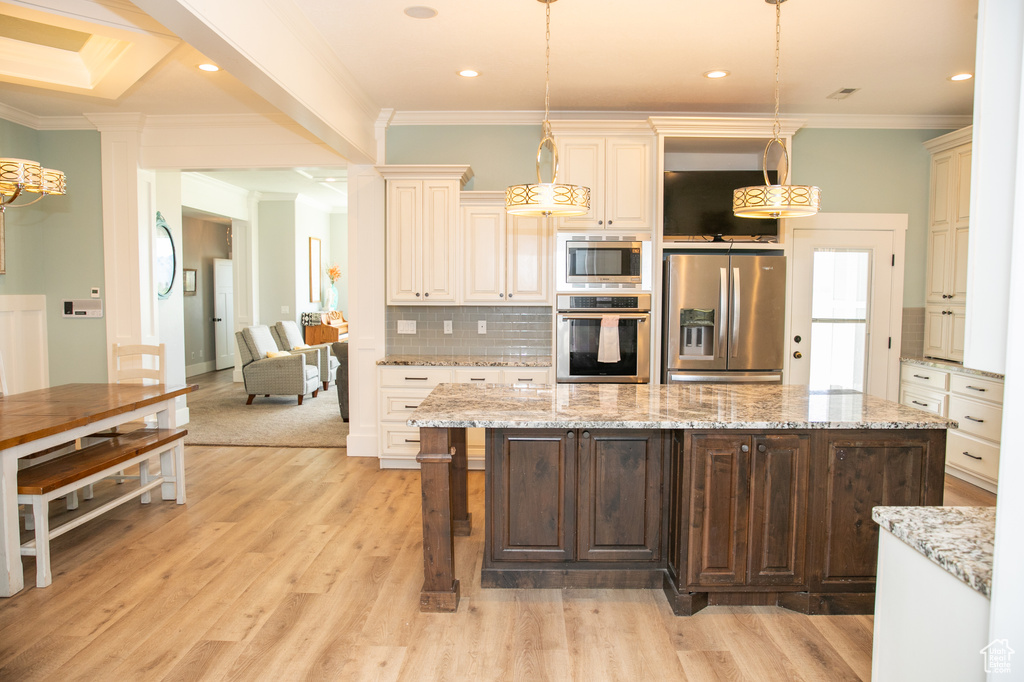 Kitchen with appliances with stainless steel finishes, light wood-type flooring, ornamental molding, and decorative light fixtures