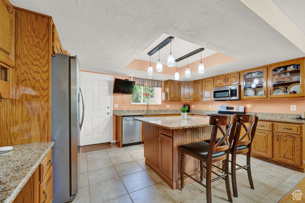 Kitchen featuring light tile patterned floors, a textured ceiling, a center island, a tray ceiling, and appliances with stainless steel finishes