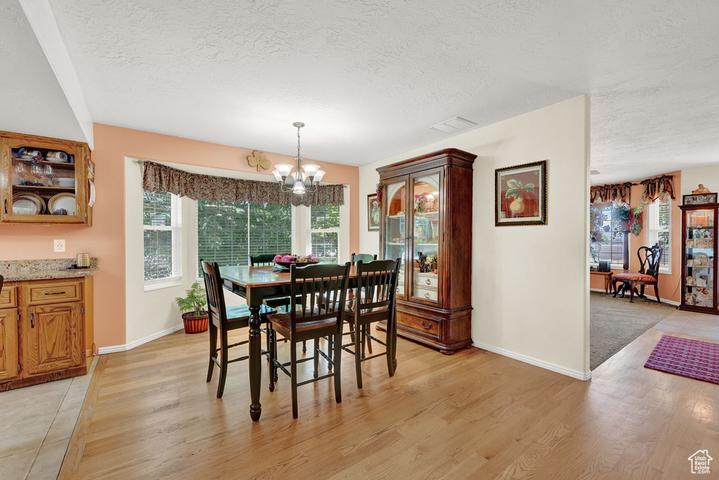 Dining space with a chandelier, a textured ceiling, and light hardwood / wood-style flooring