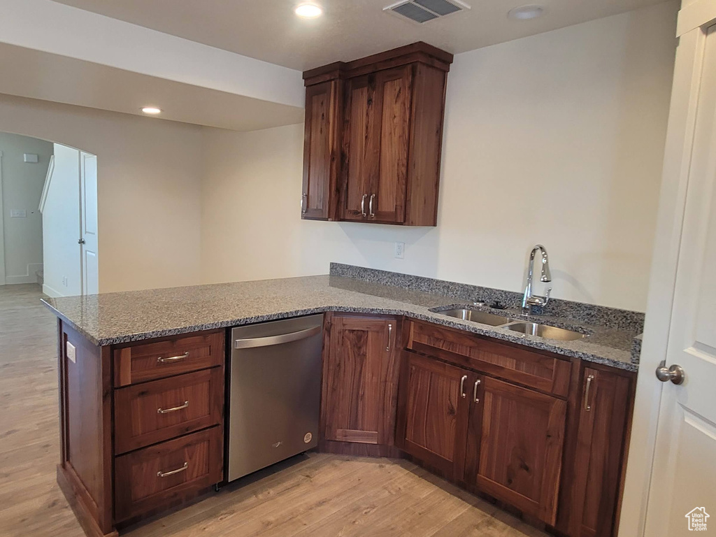 Kitchen with dishwasher, dark stone countertops, light hardwood / wood-style flooring, and sink