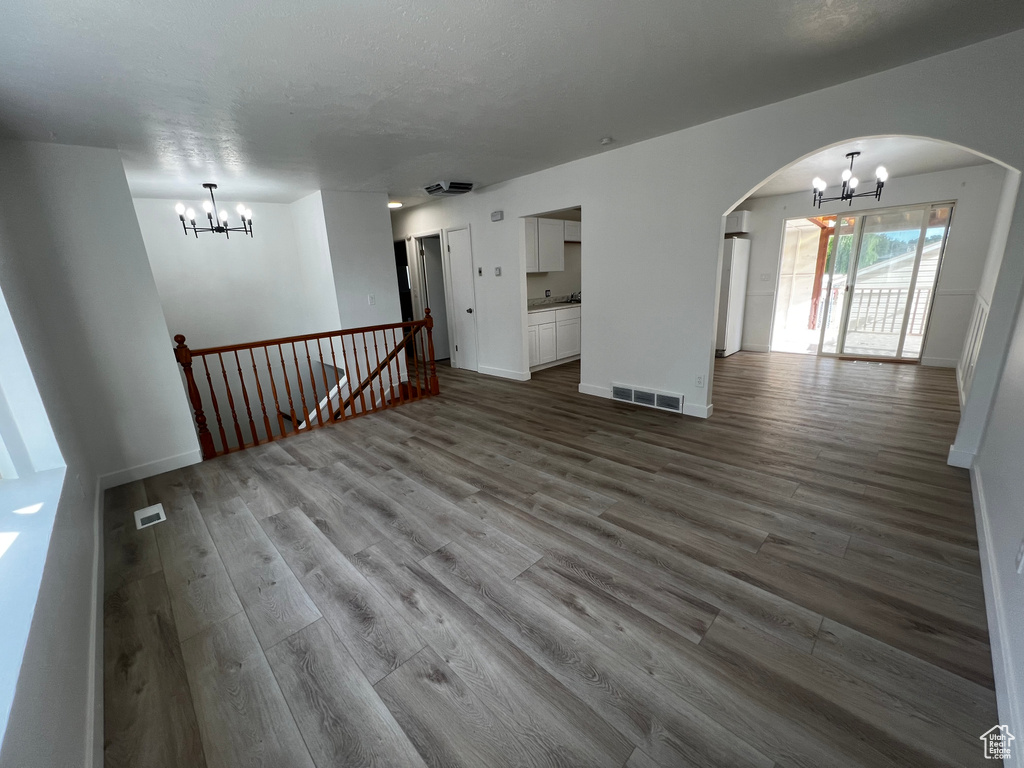 Unfurnished living room featuring wood-type flooring and a chandelier