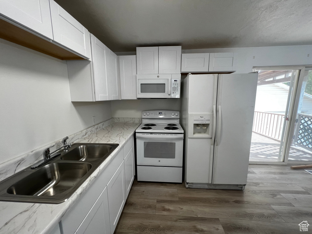 Kitchen with white cabinets, wood-type flooring, white appliances, and sink