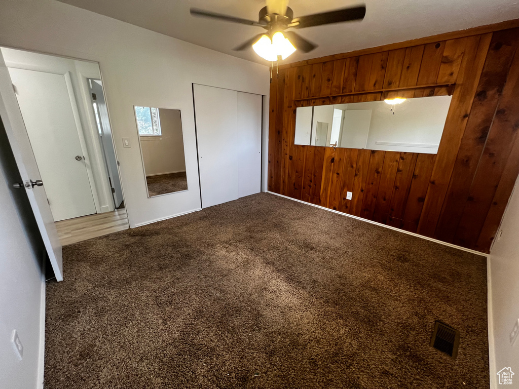 Unfurnished bedroom with wood walls, a closet, carpet floors, and ceiling fan